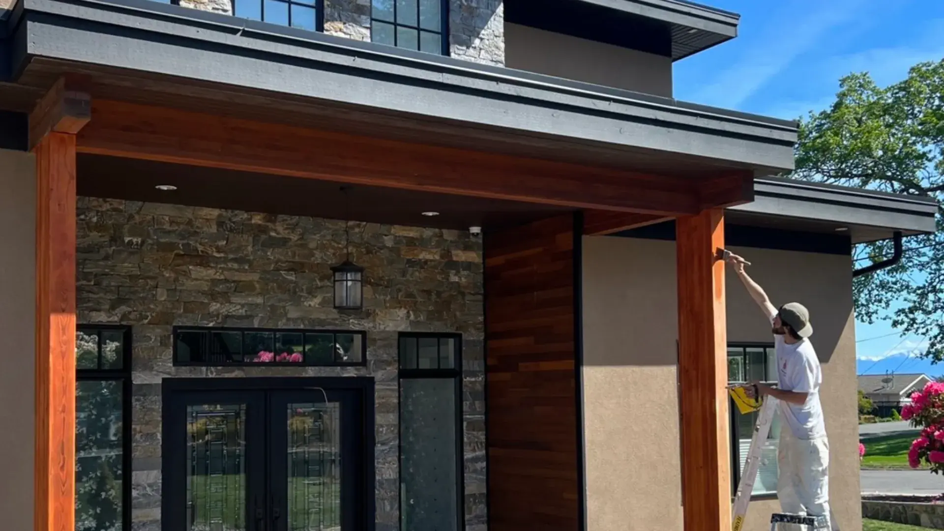 Exterior painting — painter cutting in cedar trim on a modern home